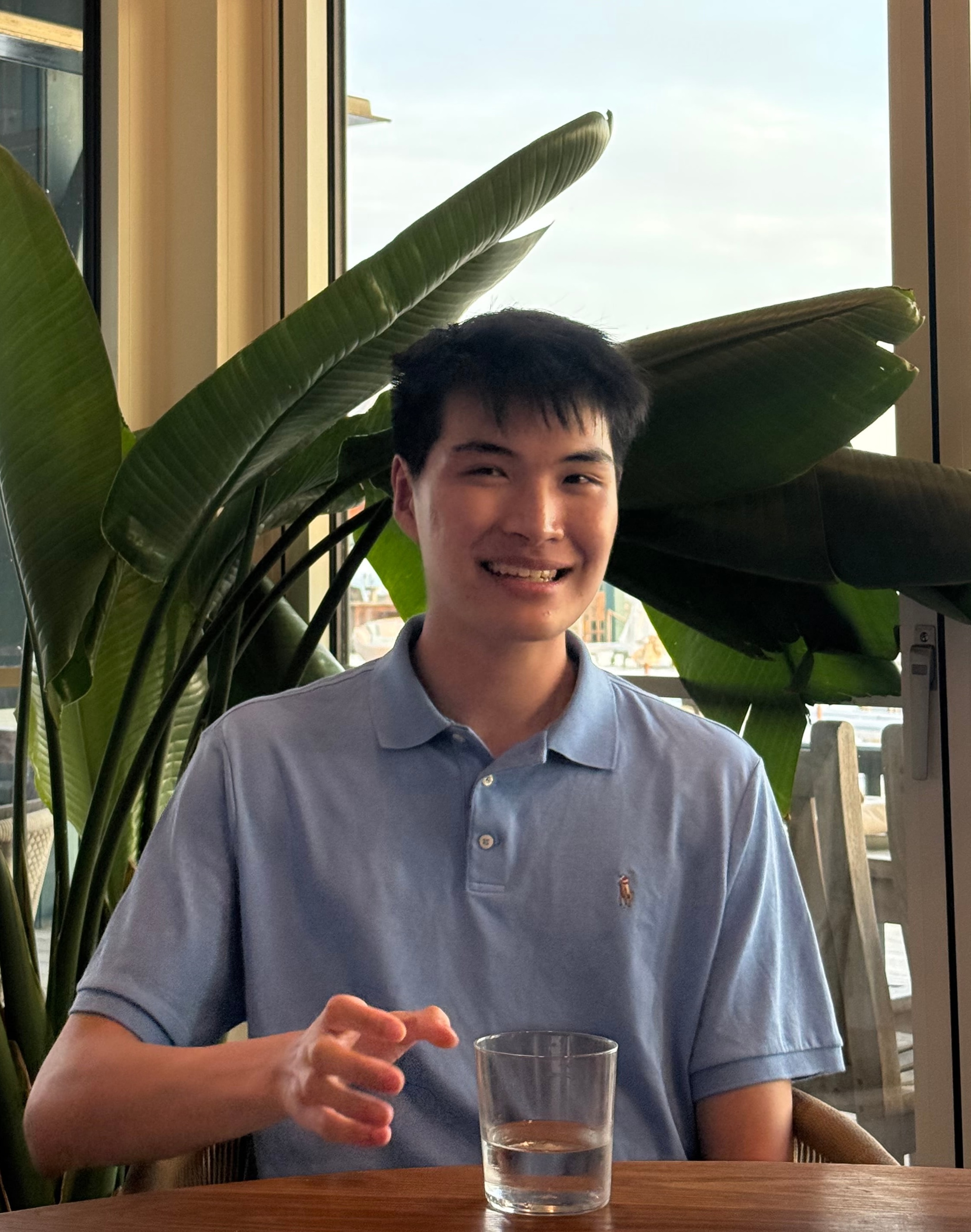 Ronnie Wang sitting near large green plants by a window
